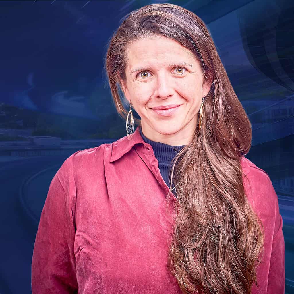 Eine Frau mit langen braunen Haaren lächelt in die Kamera vor einem futuristischen Hintergrund.