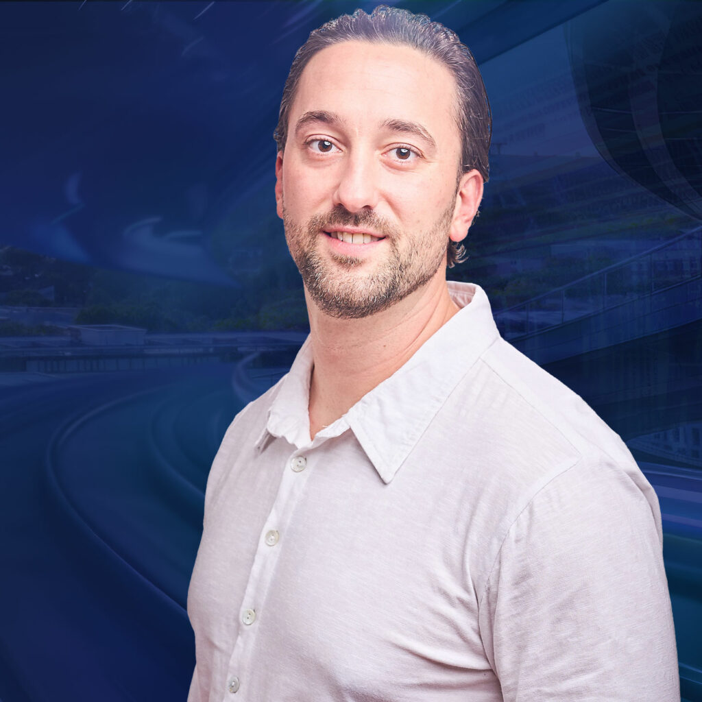 Ein Mann in einem weißen Hemd lächelt in die Kamera vor einem futuristischen blauen Hintergrund.