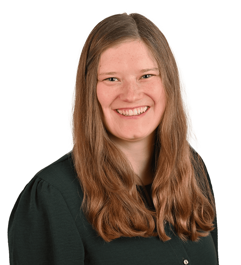 Eine lächelnde Frau mit langen braunen Haaren, die eine dunkelgrüne Bluse trägt.