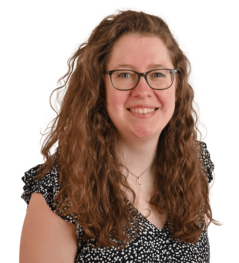 Eine lächelnde Frau mit langen braun gelockten Haaren und einer Brille.