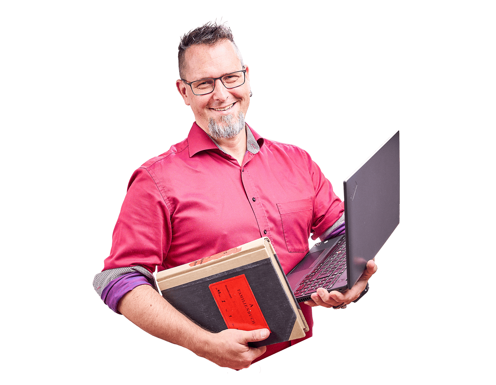 Lächender Mann mit rotem T-Shirt, Brille und Bärtchen hält einen Laptop und ein Buch in seinen Händen