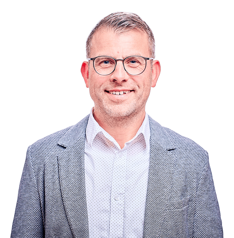 Ein lächelnder Mann, der eine Brille, ein weißes Hemd und einen grauen Blaser trägt.