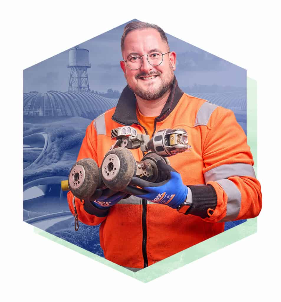 Ein lächelnder Mann, der in orangener Arbeitskleidung vor einem futuristischen Hintergrund steht.