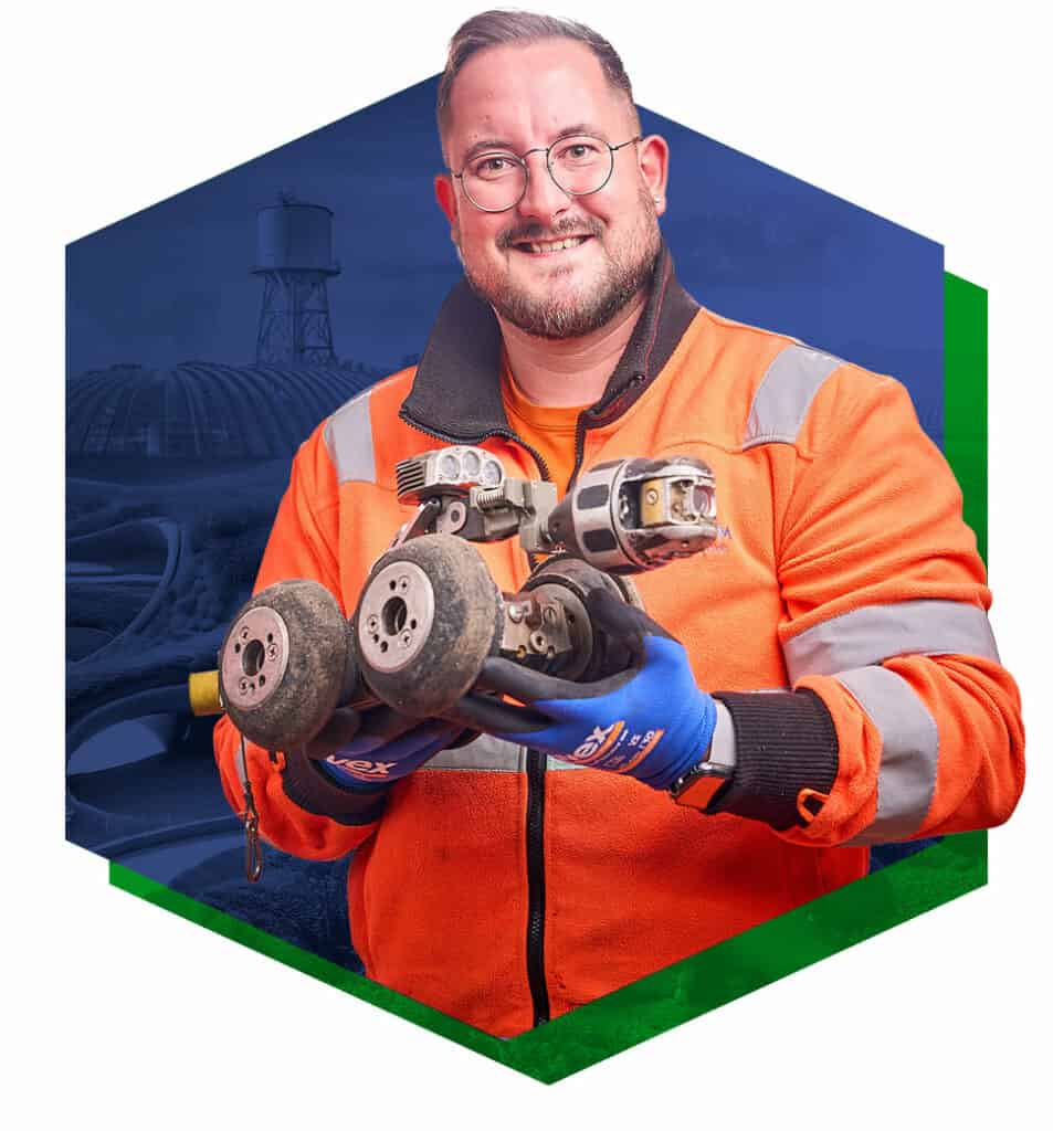 Ein lächelnder Mann, der in orangener Arbeitskleidung vor einem futuristischen Hintergrund steht.