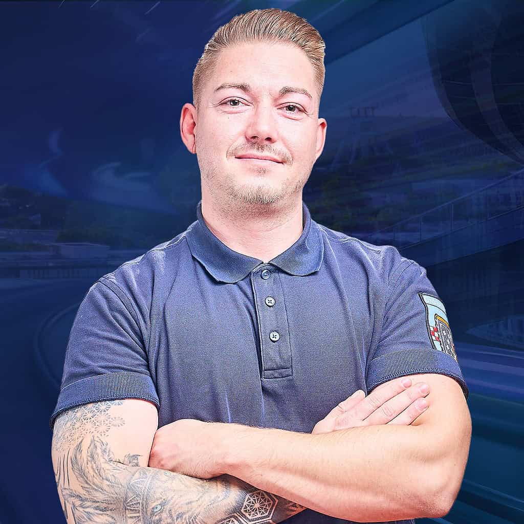 Ein tätowierter Mann in einem blauen T-Shirt schaut lächelnt in die Kamera.