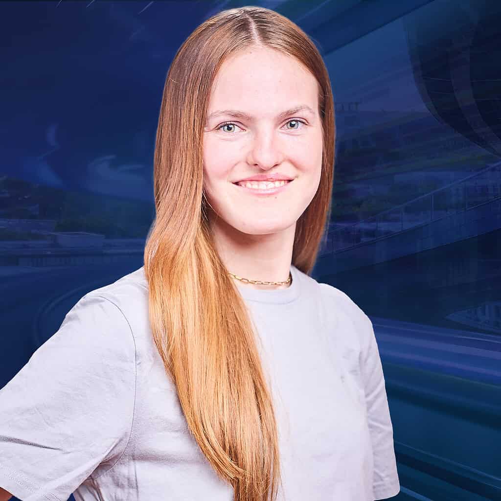 Eine lächelnde Frau in weißem T-Shirt steht vor einem verschwommenen blauen Hintergrund.